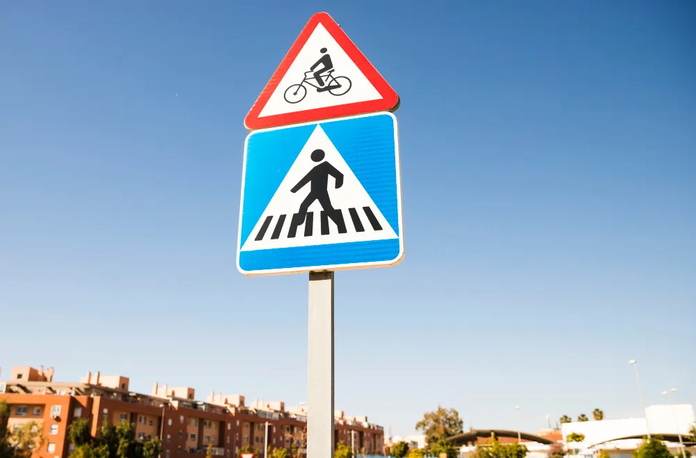 Dreieckiges Fahrrad-Warnschild über einem quadratischen Fußgängerüberweg-Schild in der Stadt