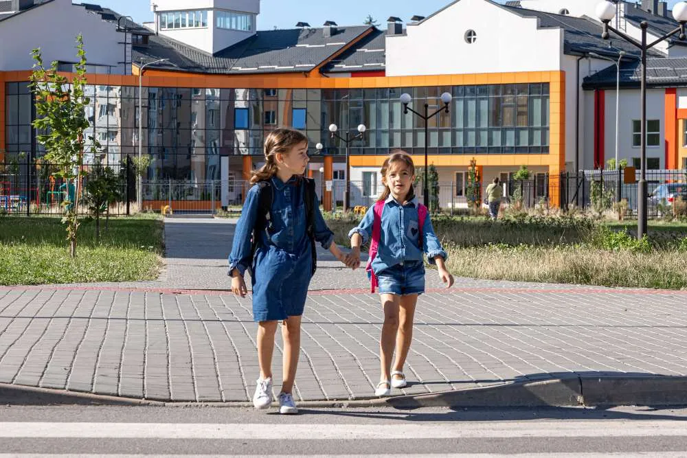 Deux écolières traversant la rue devant une école moderne avec sacs à dos
