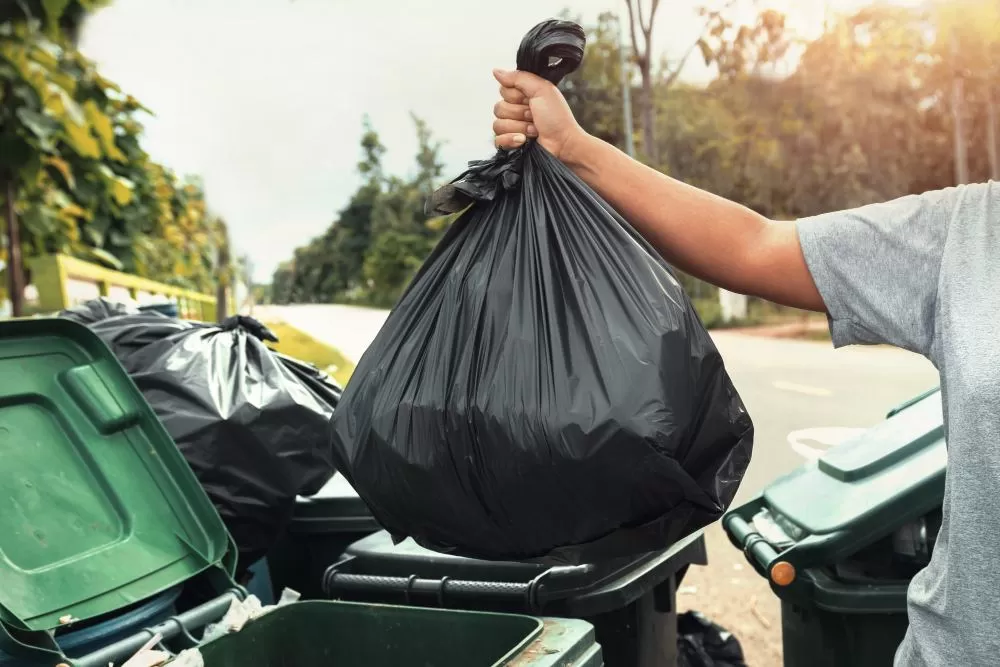 Femme tenant à la main des déchets dans un sac noir pour les nettoyer à la poubelle