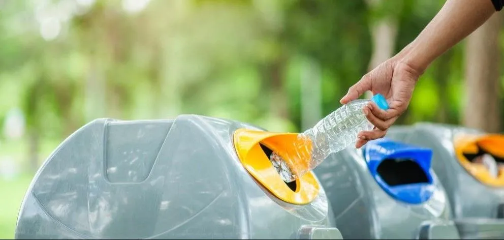 persoon die een fles in een prullenbak gooit