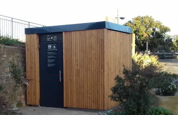 Openbare toiletten met een houten gevel omringd door struiken.